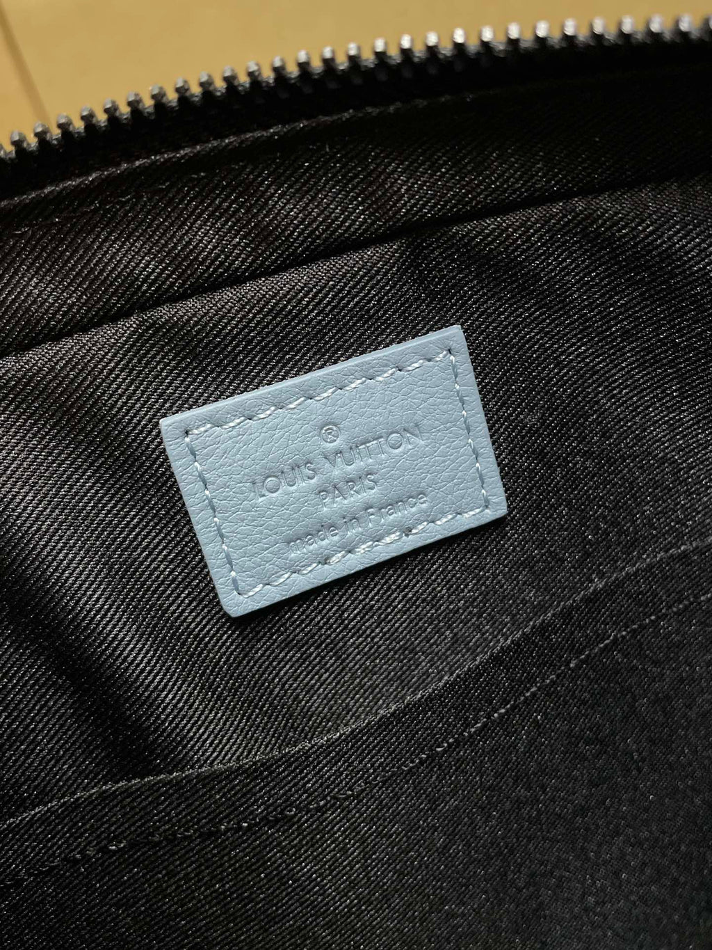 Light blue logo patch on black interior fabric of monogram crossbody bag