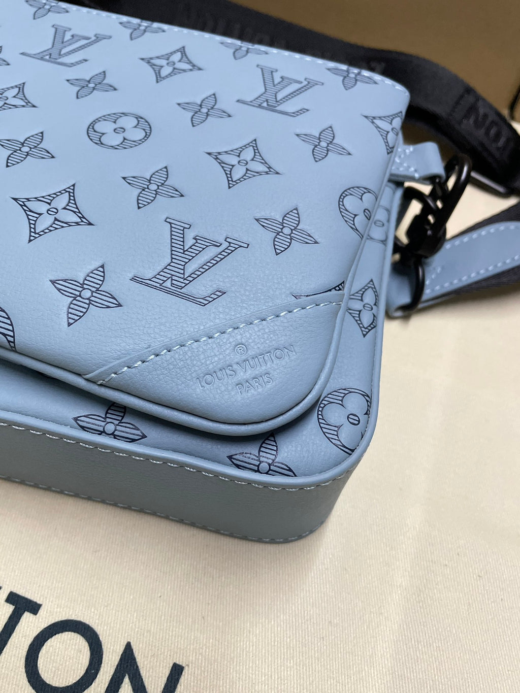 Close-up of light blue monogram crossbody bag corner with stitched trim