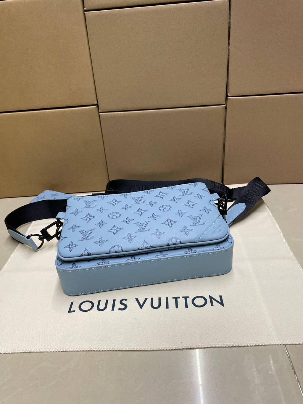 Light blue monogram crossbody bag with black strap and matching pouch accessory