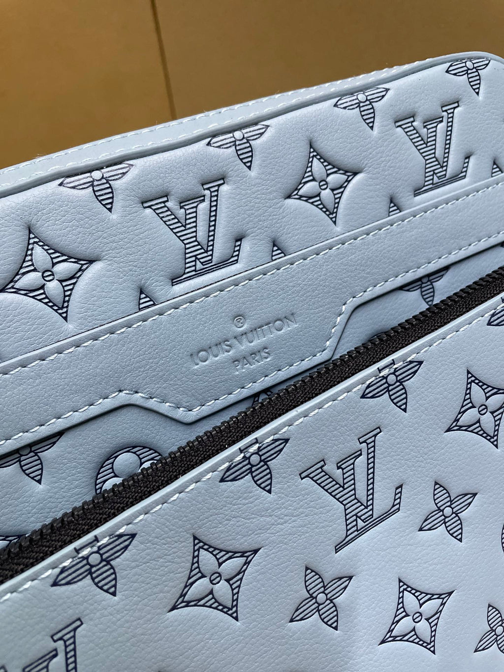 Close-up of light blue monogram crossbody bag with embossed branding