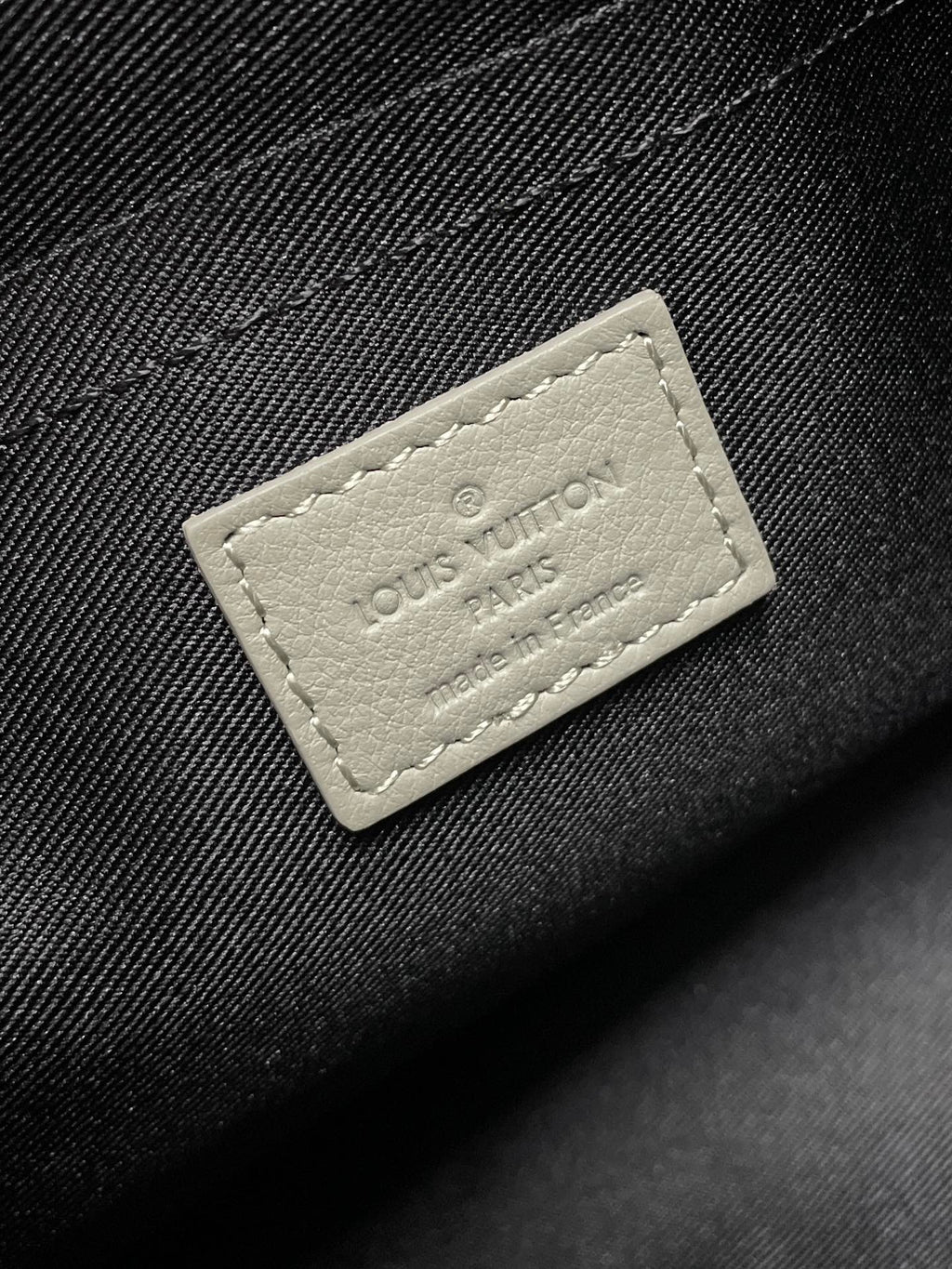 Louis Vuitton strap patch, small light leather label on dark fabric with branding