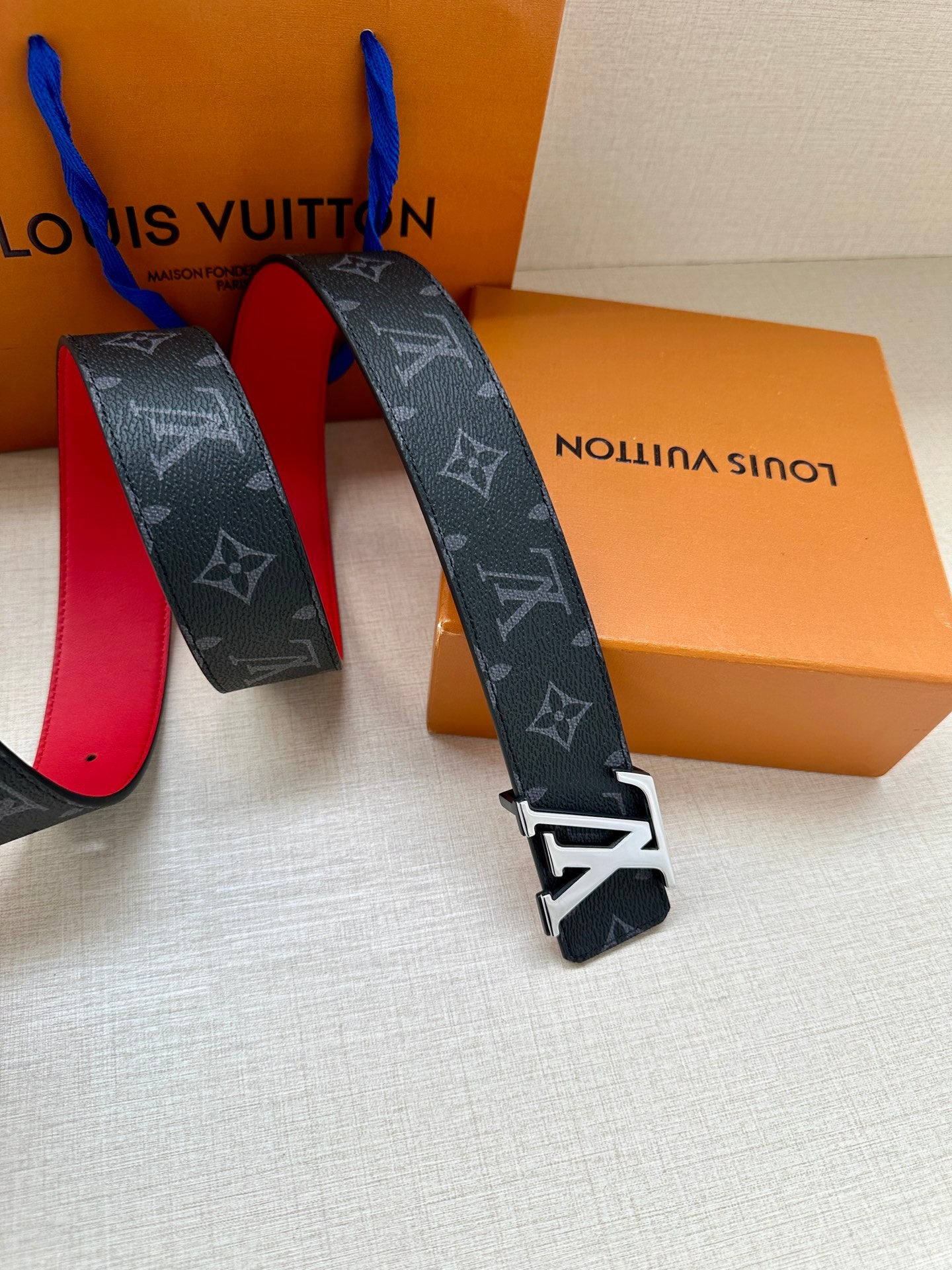 Navy monogram belt with metal buckle hardware and red-lined underside