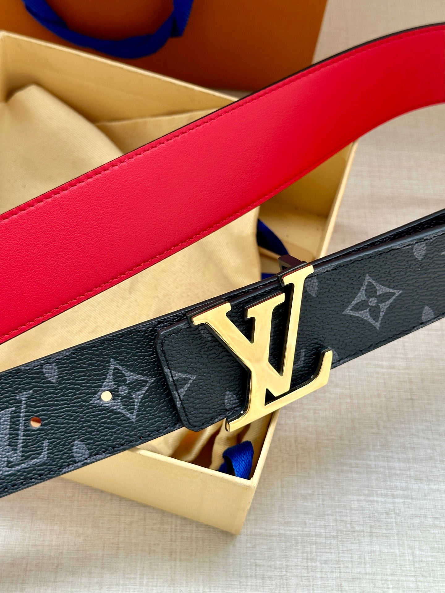 Navy monogram belt close-up with gold LV buckle and red-lined leather