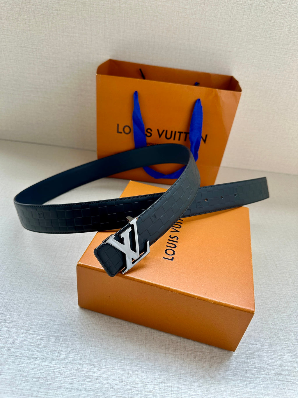 Blue embossed leather belt with silver LV logo buckle and strap end detail.