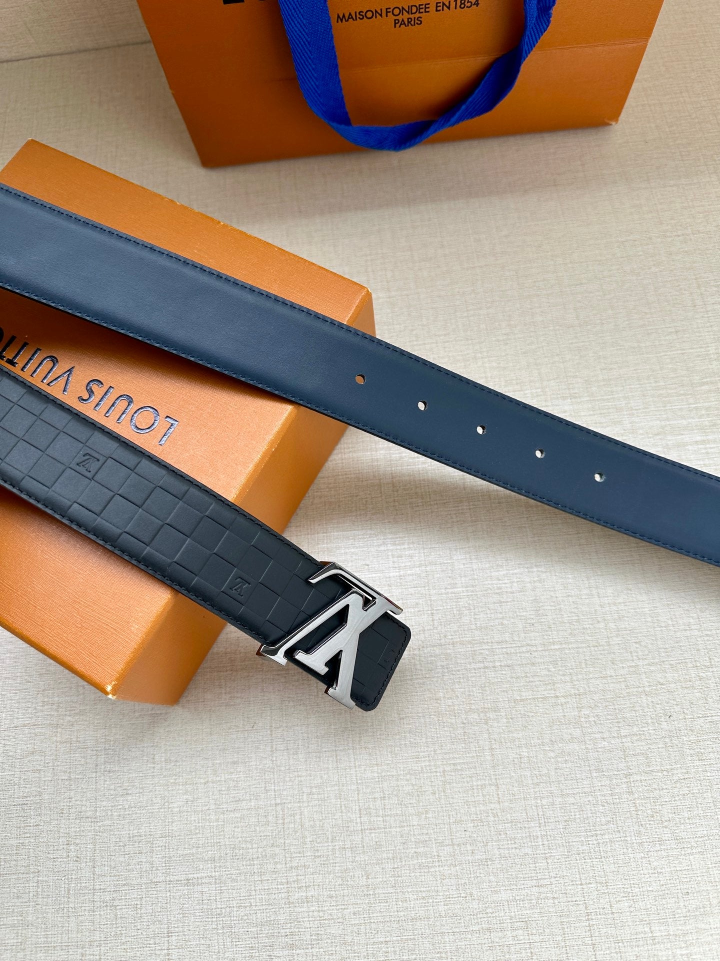 Blue embossed leather belt with silver prong buckle and punched adjustment holes.