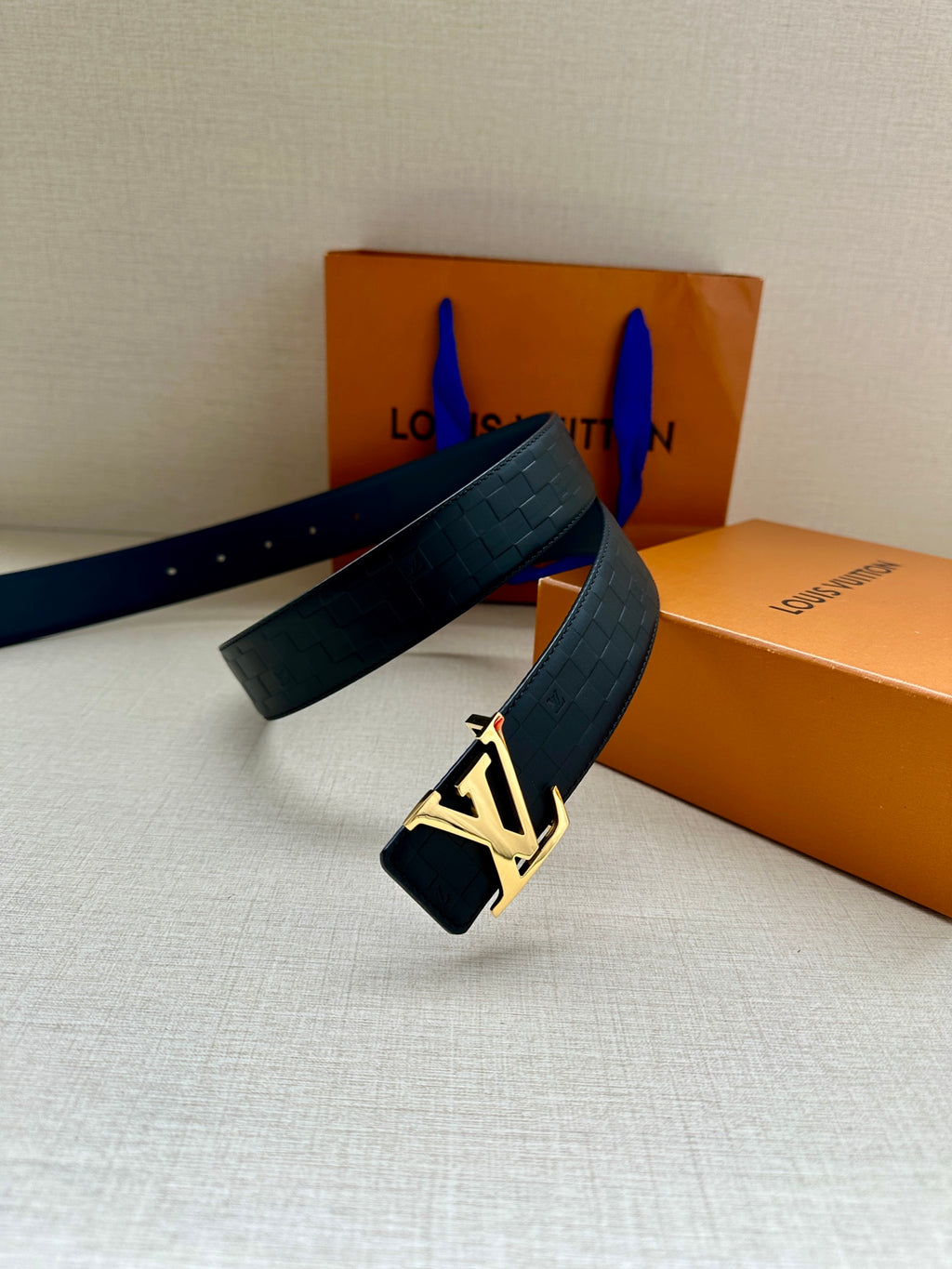 Blue embossed leather belt with gold-tone LV logo buckle and looped strap.