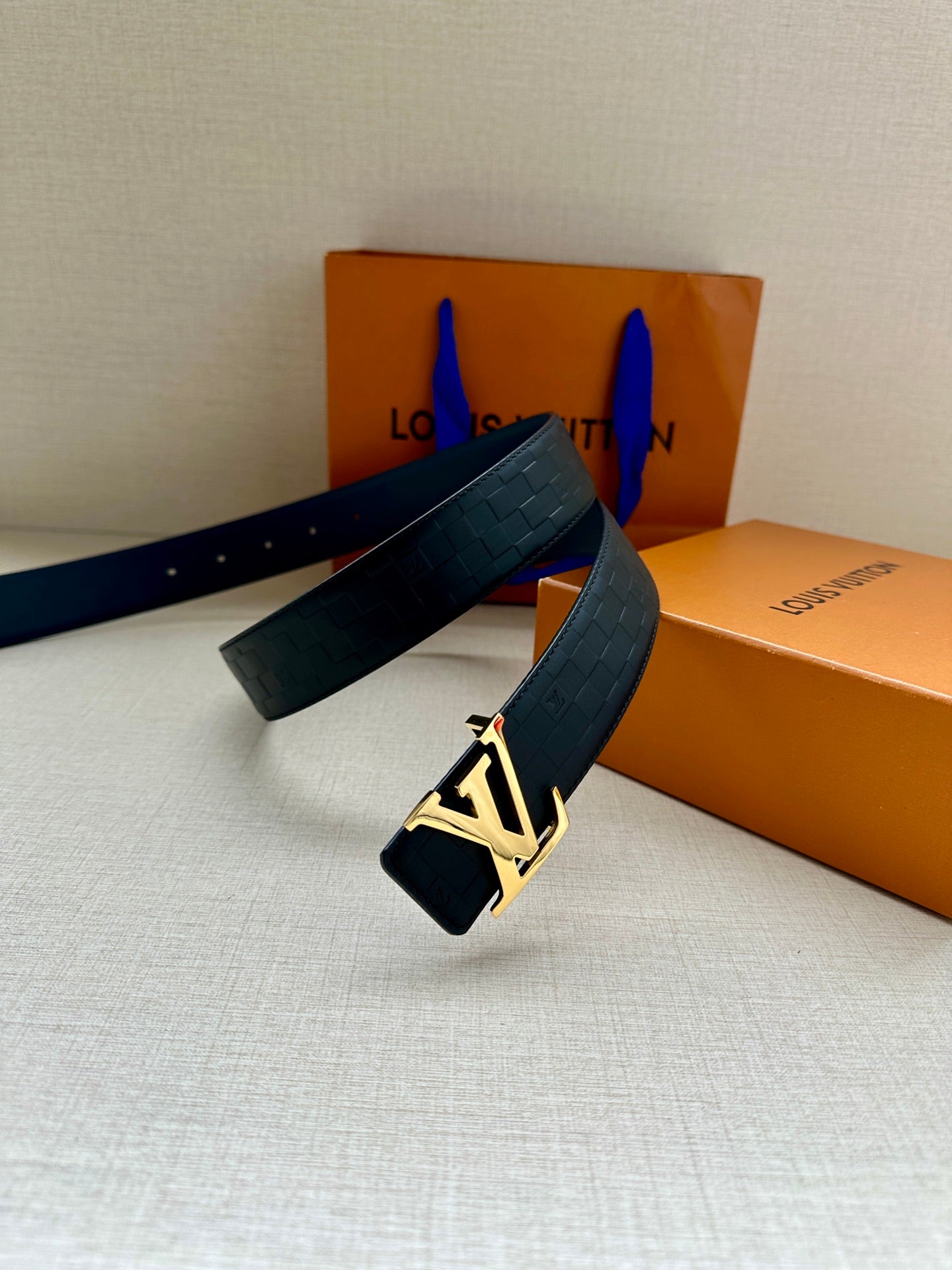 Blue embossed leather belt with gold-tone LV logo buckle and looped strap.