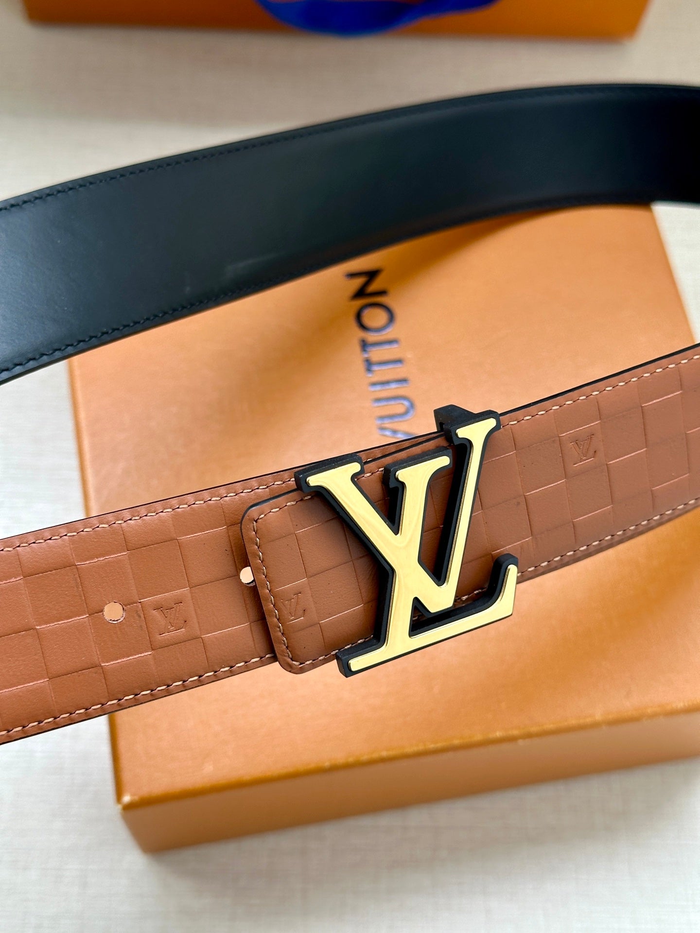 Louis Vuitton tan belt with embossed texture and gold-tone LV buckle close-up