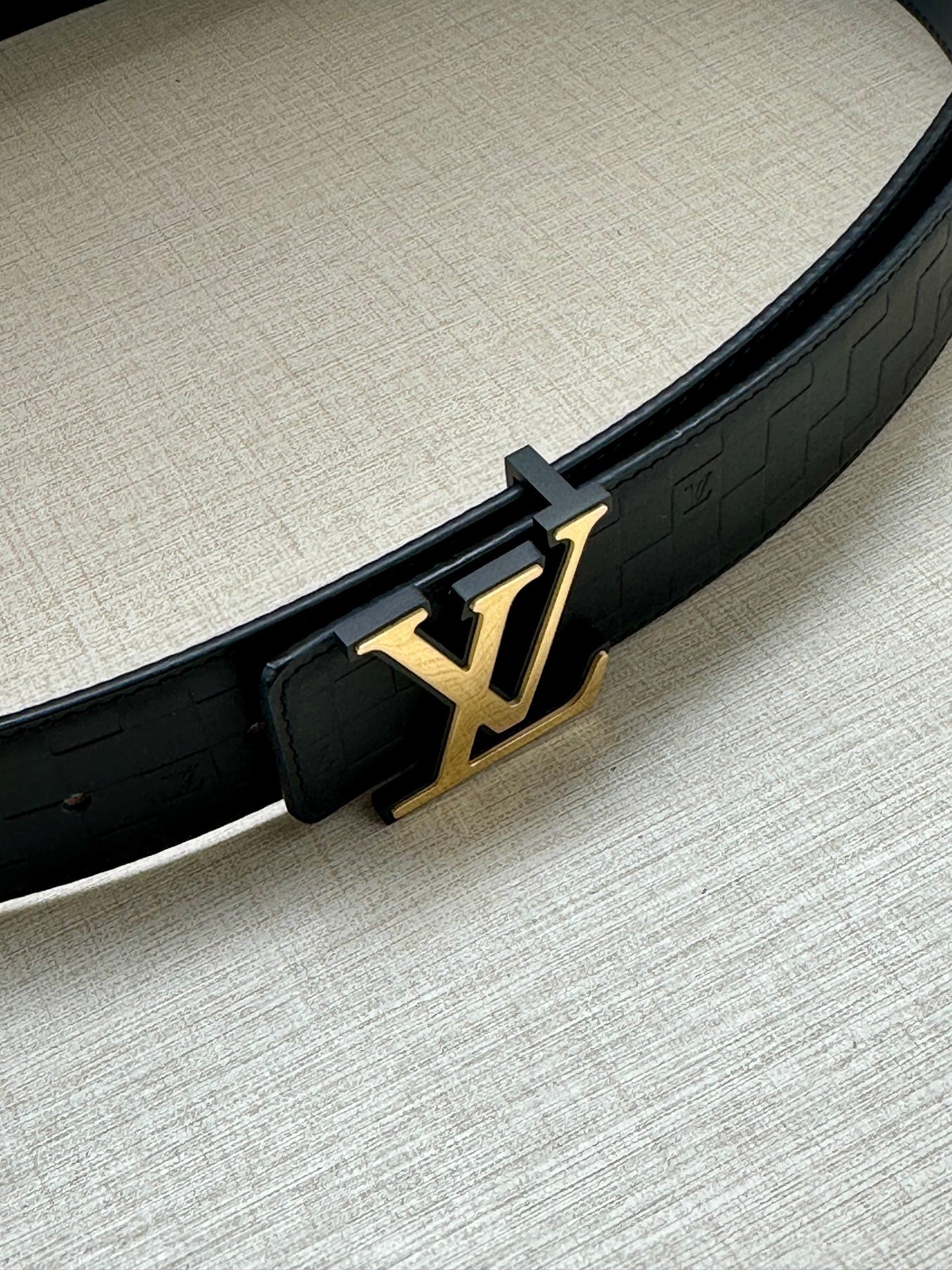 Louis Vuitton belt detail: dark blue strap with gold LV buckle and embossed texture