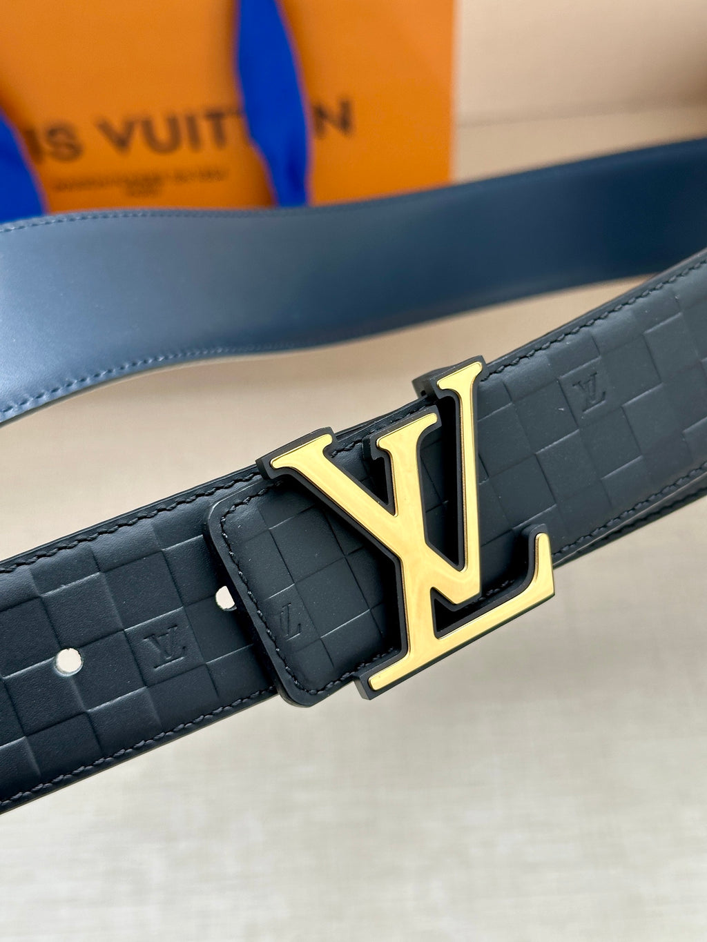 Louis Vuitton belt close-up: embossed dark blue strap with gold LV buckle