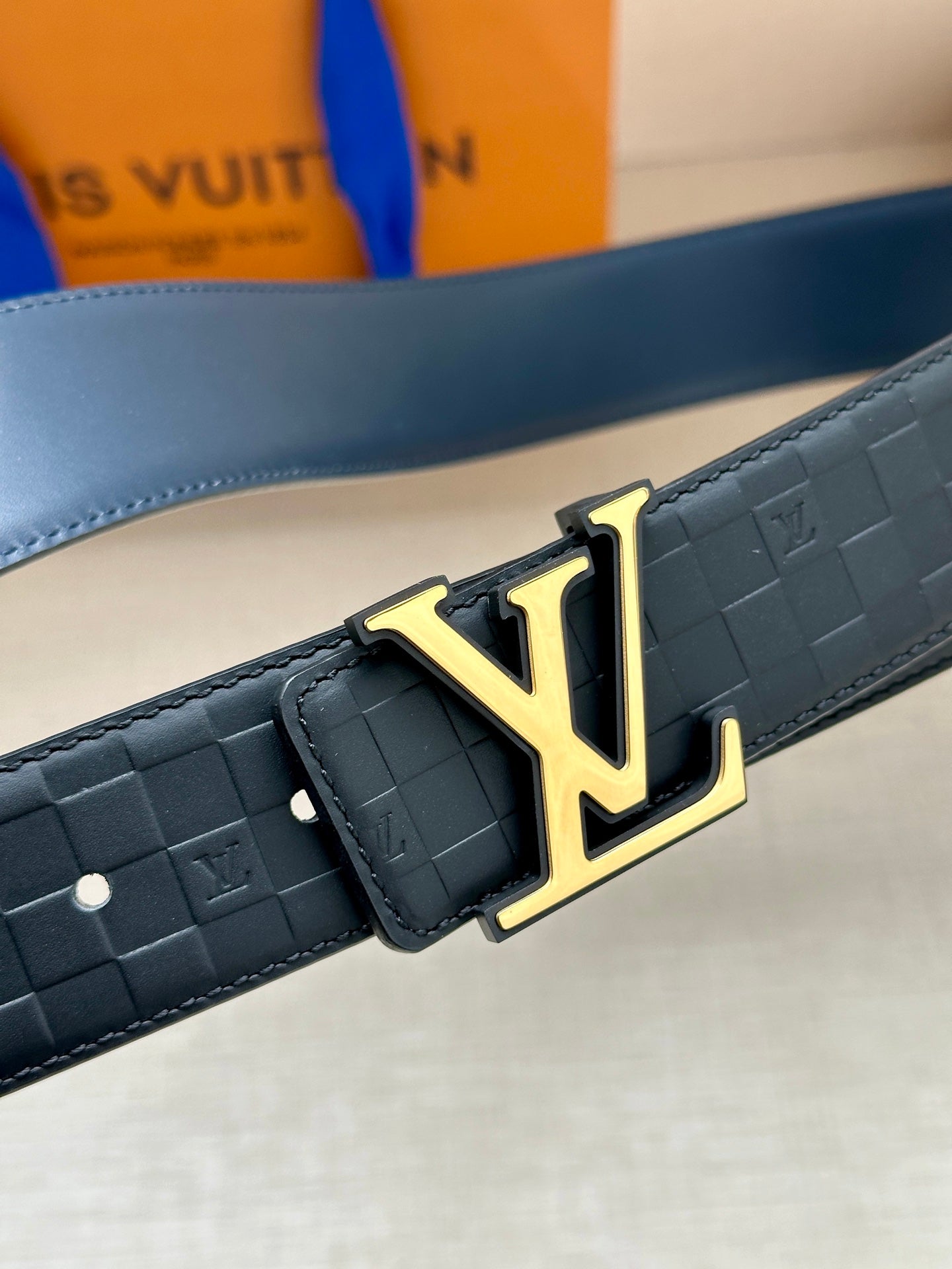 Louis Vuitton belt close-up: embossed dark blue strap with gold LV buckle