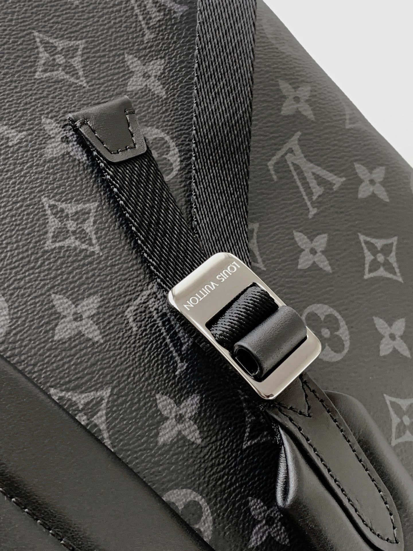 Close-up of adjustable strap and metal connector on dark monogram backpack