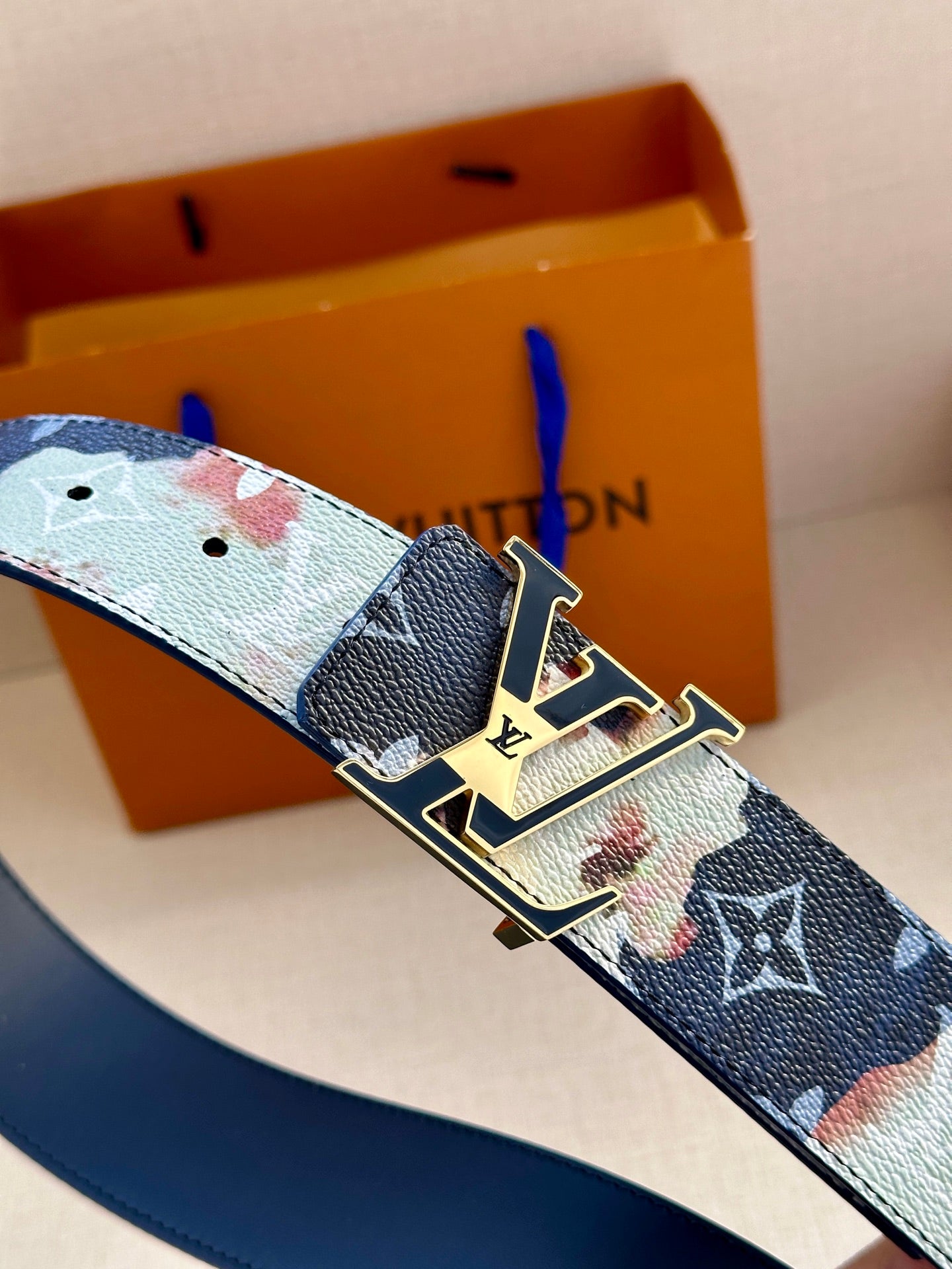 Monogram belt with blue strap, light trim, and gold-tone buckle clasp.