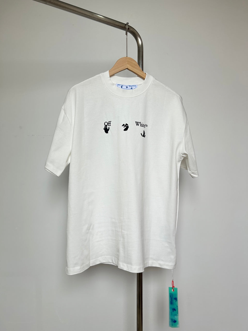 Off-white T-shirt with small blue-and-black graphic icons on chest