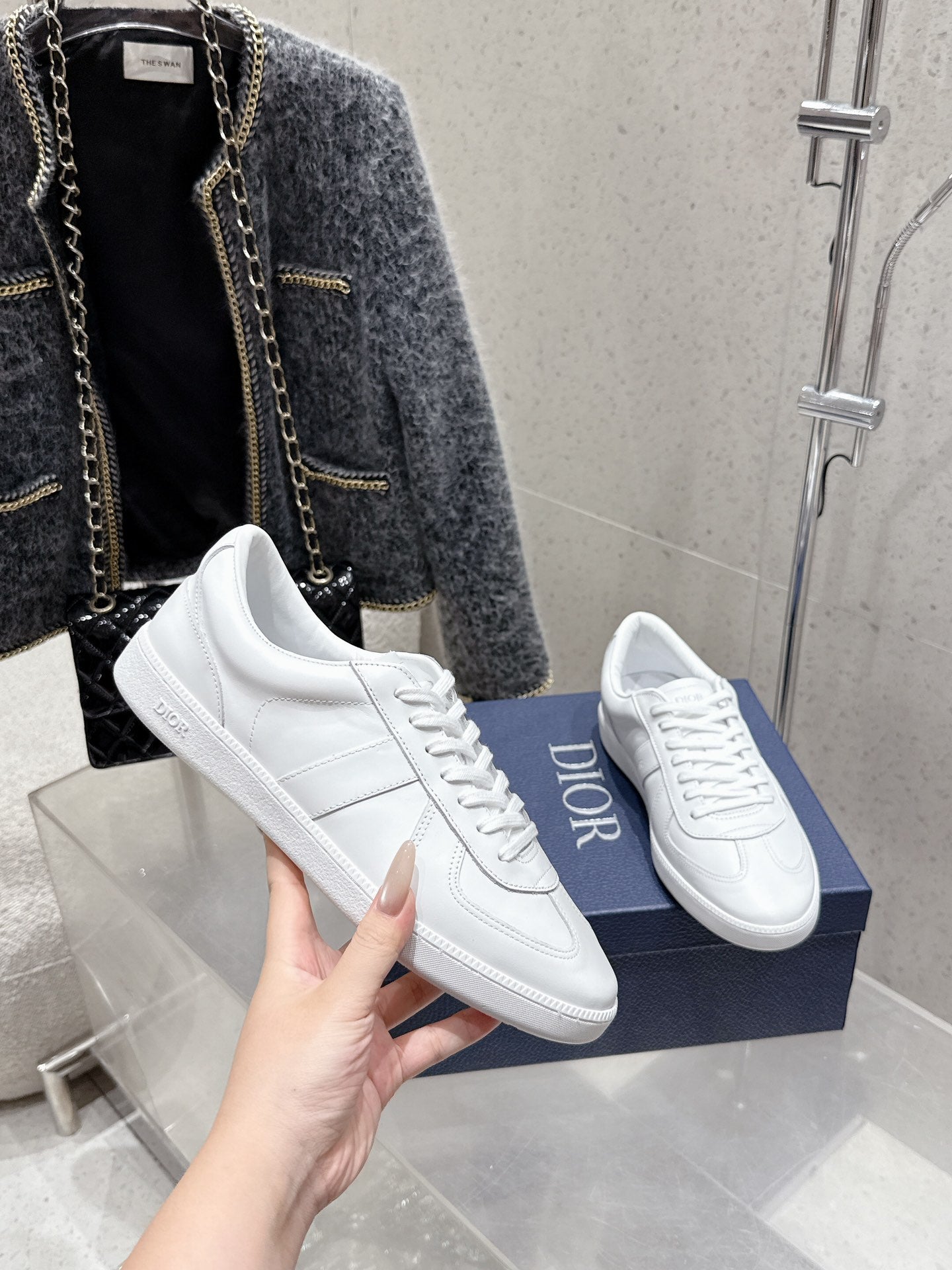 Hand holding white Dior unisex sneakers on blue box, lace-up with sole