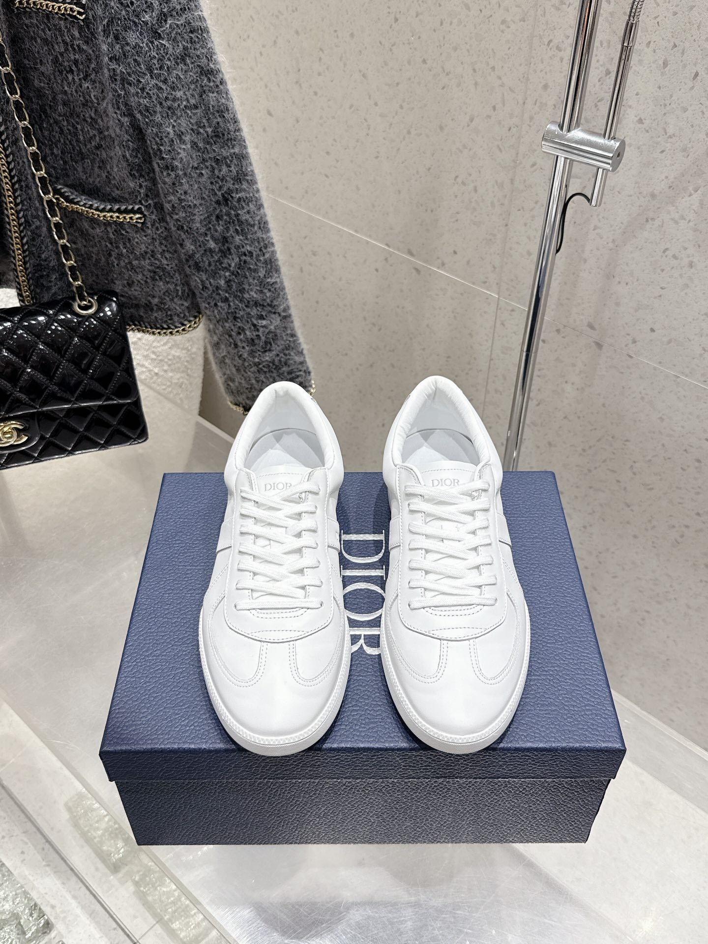 White Dior unisex sneakers on blue box, lace-up with stitched panels