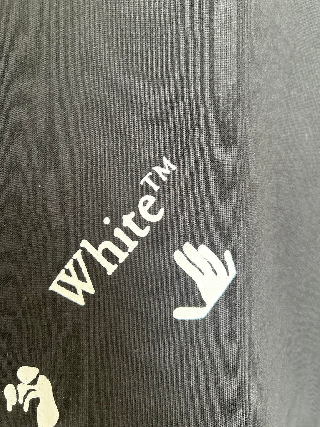 Black T-shirt sleeve close-up with White TM text and hand logo