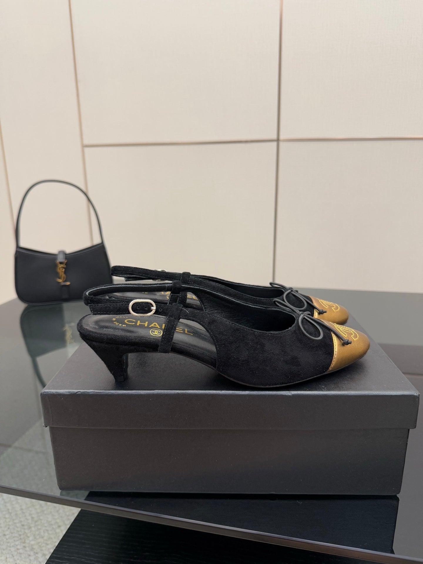 Black suede sling-back ballet flat with gold toe cap and bow laces, side view.