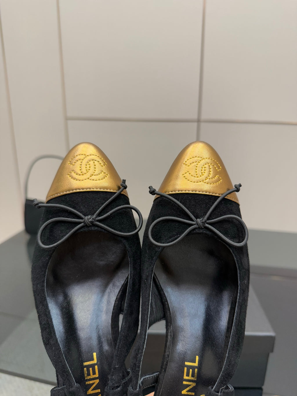 Close-up of black suede ballet flats with gold toe caps and bow laces.