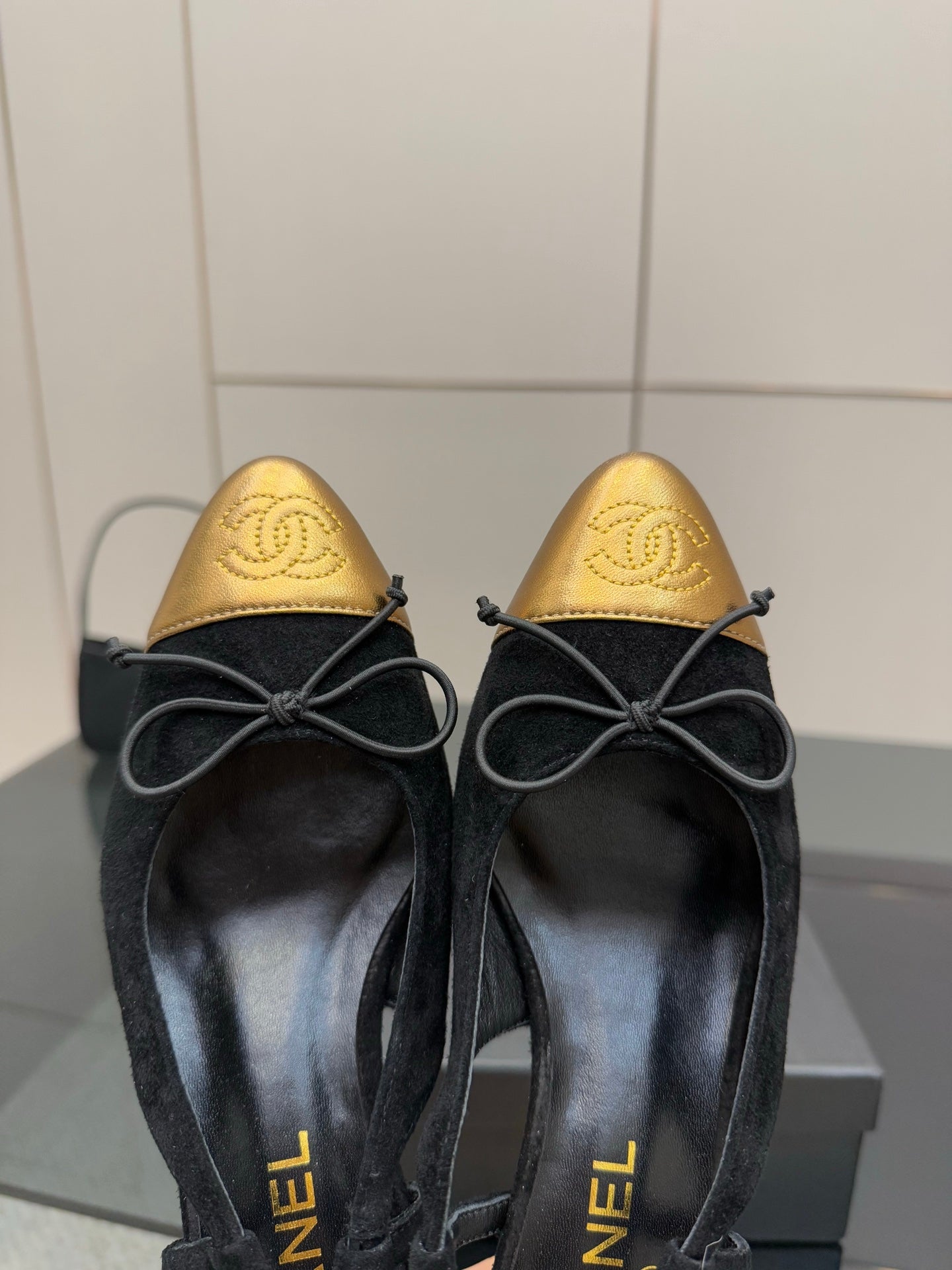 Close-up of black suede ballet flats with gold toe caps and bow laces.
