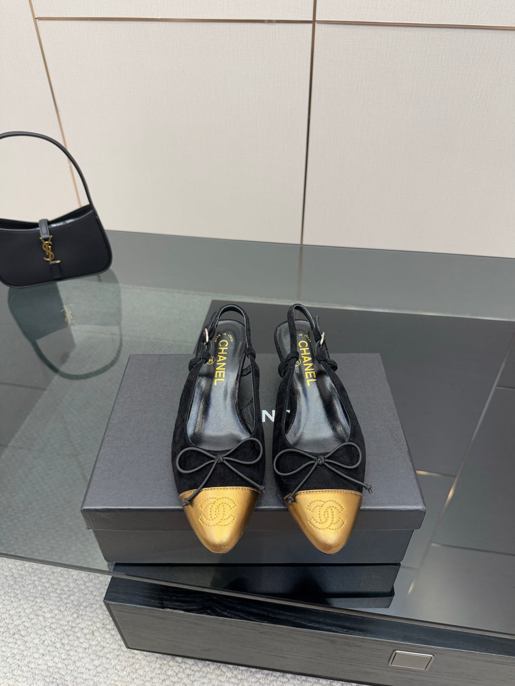 Black and gold toe cap ballet flats, laced bows, shown on a shoe box.