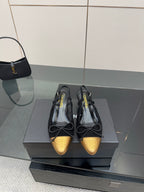 Black and gold toe cap ballet flats, laced bows, shown on a shoe box.
