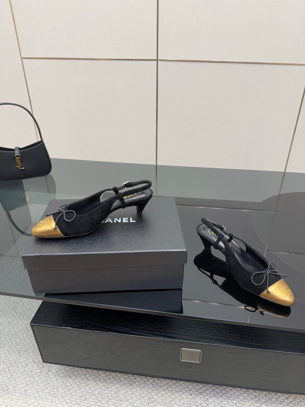 Pair of black suede ballet flats with gold toe caps and bow laces, angled view.