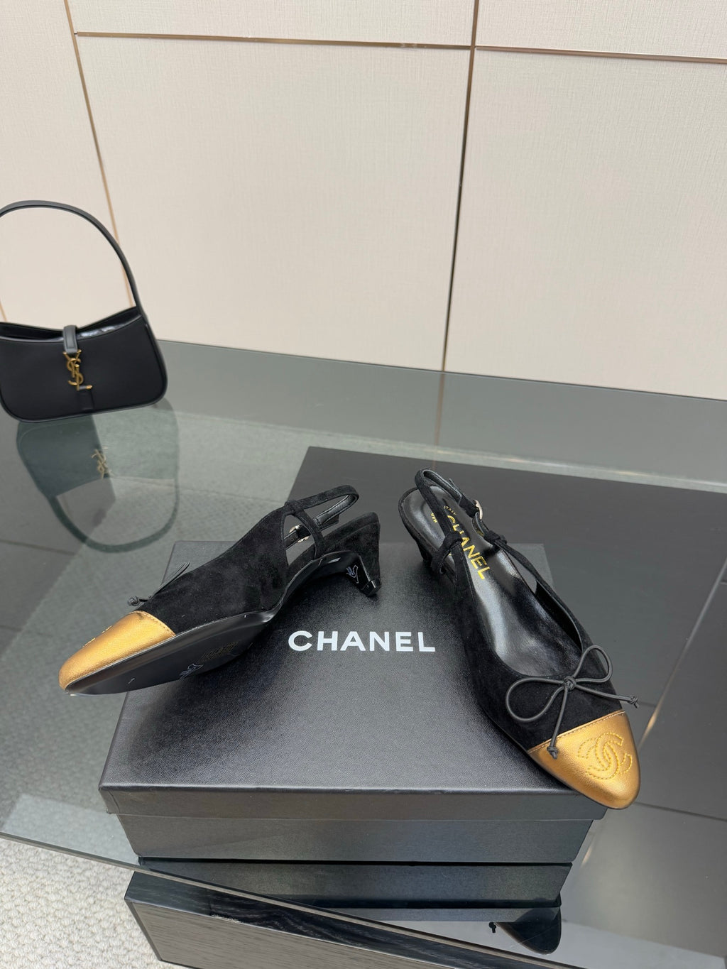 Black and gold ballet flats with bow laces, CHANEL logo visible on the shoe.