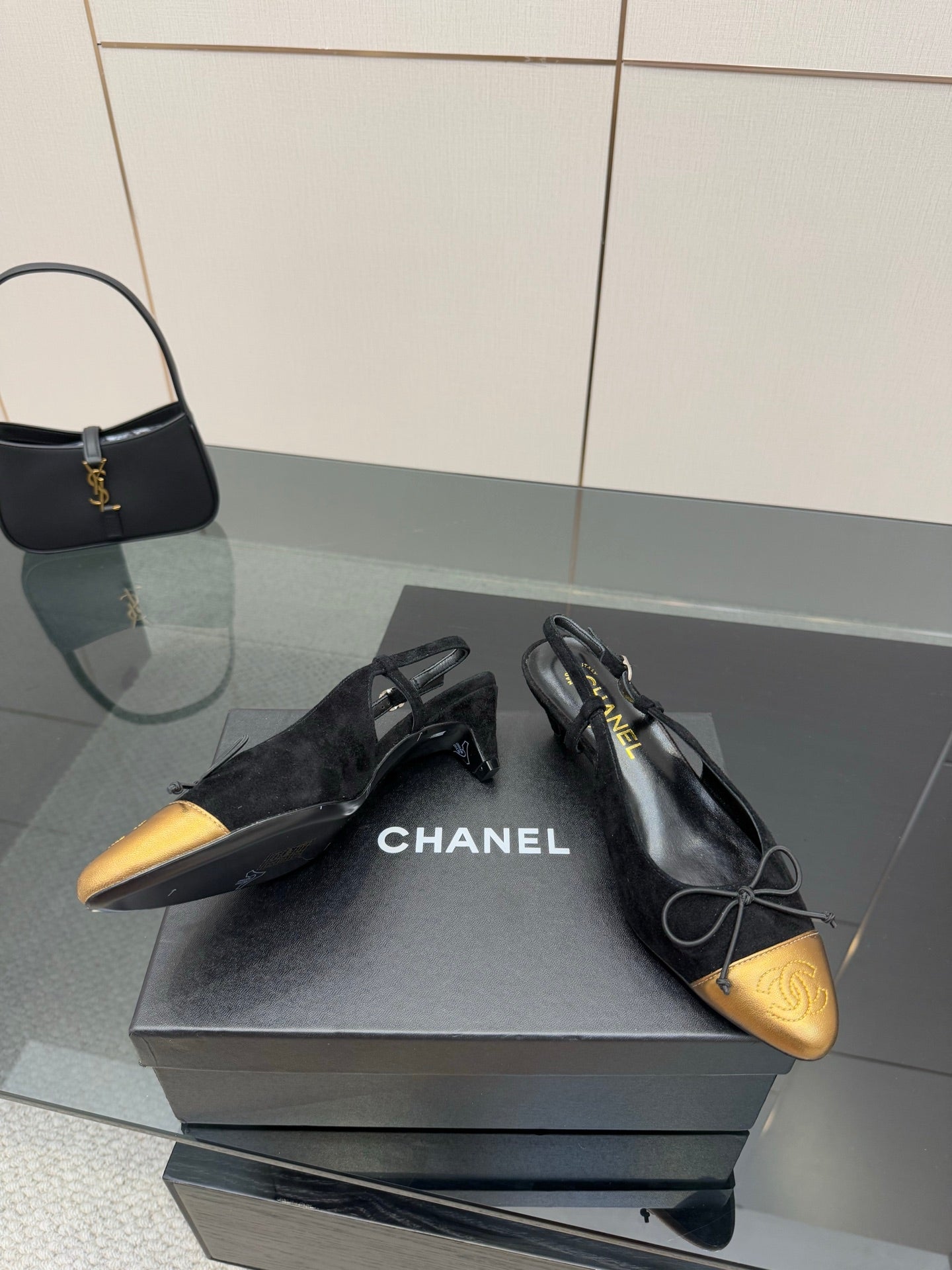Black and gold ballet flats with bow laces, CHANEL logo visible on the shoe.
