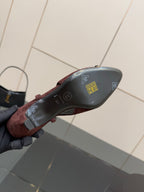 Women’s shoe outsole view, burgundy and gold upper, dark sole with printed icons.