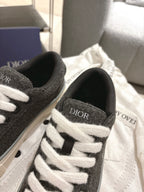 Unisex sneaker close-up: dark gray canvas, white laces, Dior logo on tongue