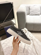 Unisex sneaker held up, dark gray upper with white laces and side text