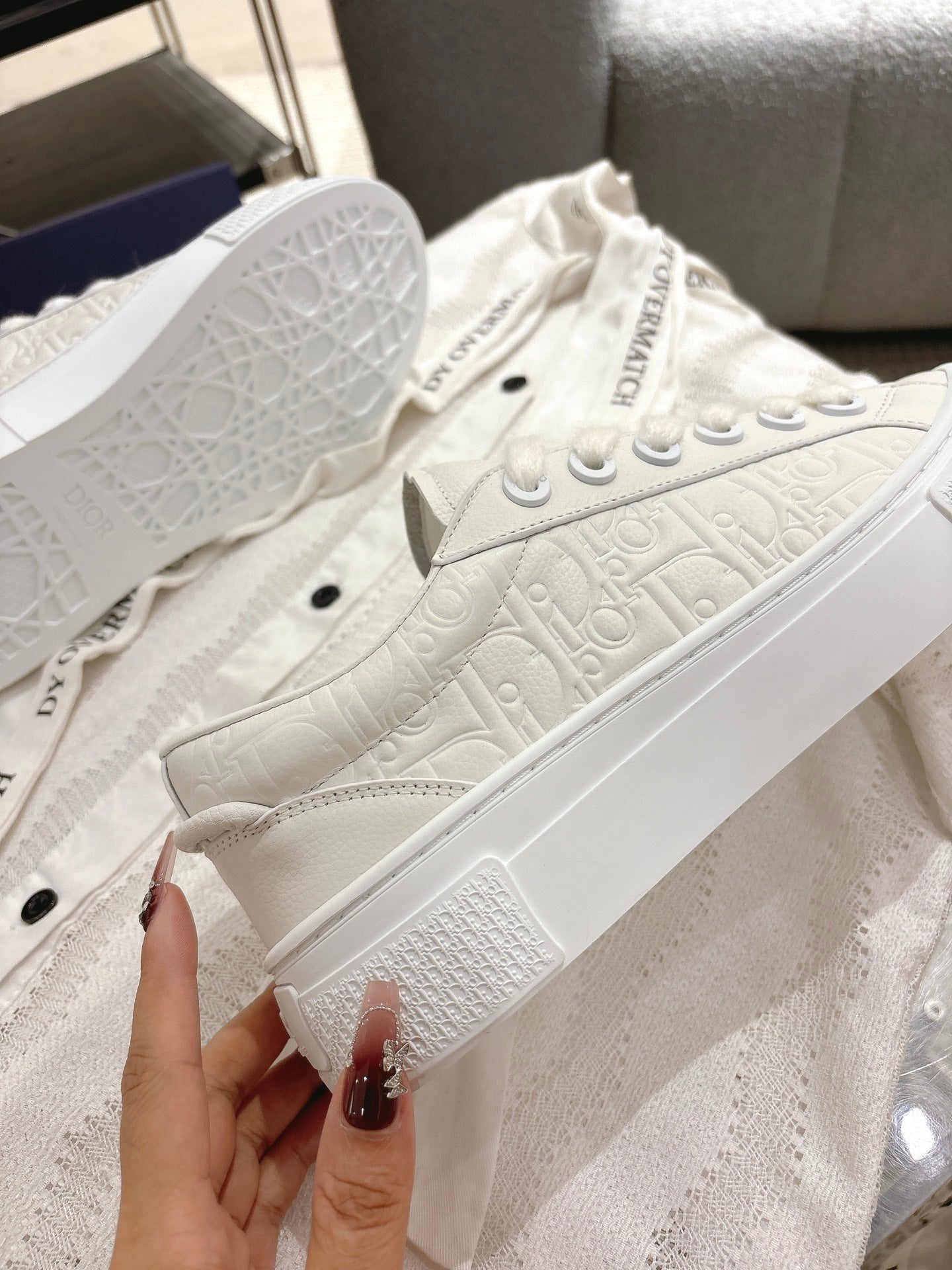 White Dior sneakers top view, lace-up eyelets and textured leather-like upper