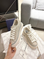 Light beige low-top sneakers with white laces and side panel embossing, held up