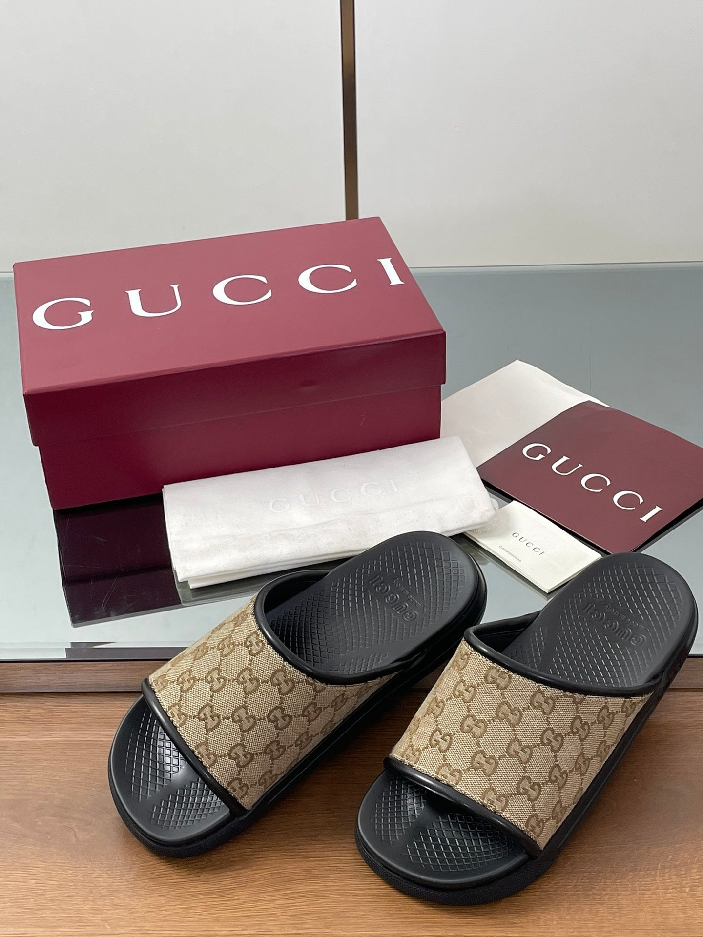 Gucci slide sandals with beige GG canvas straps over black cushioned footbeds