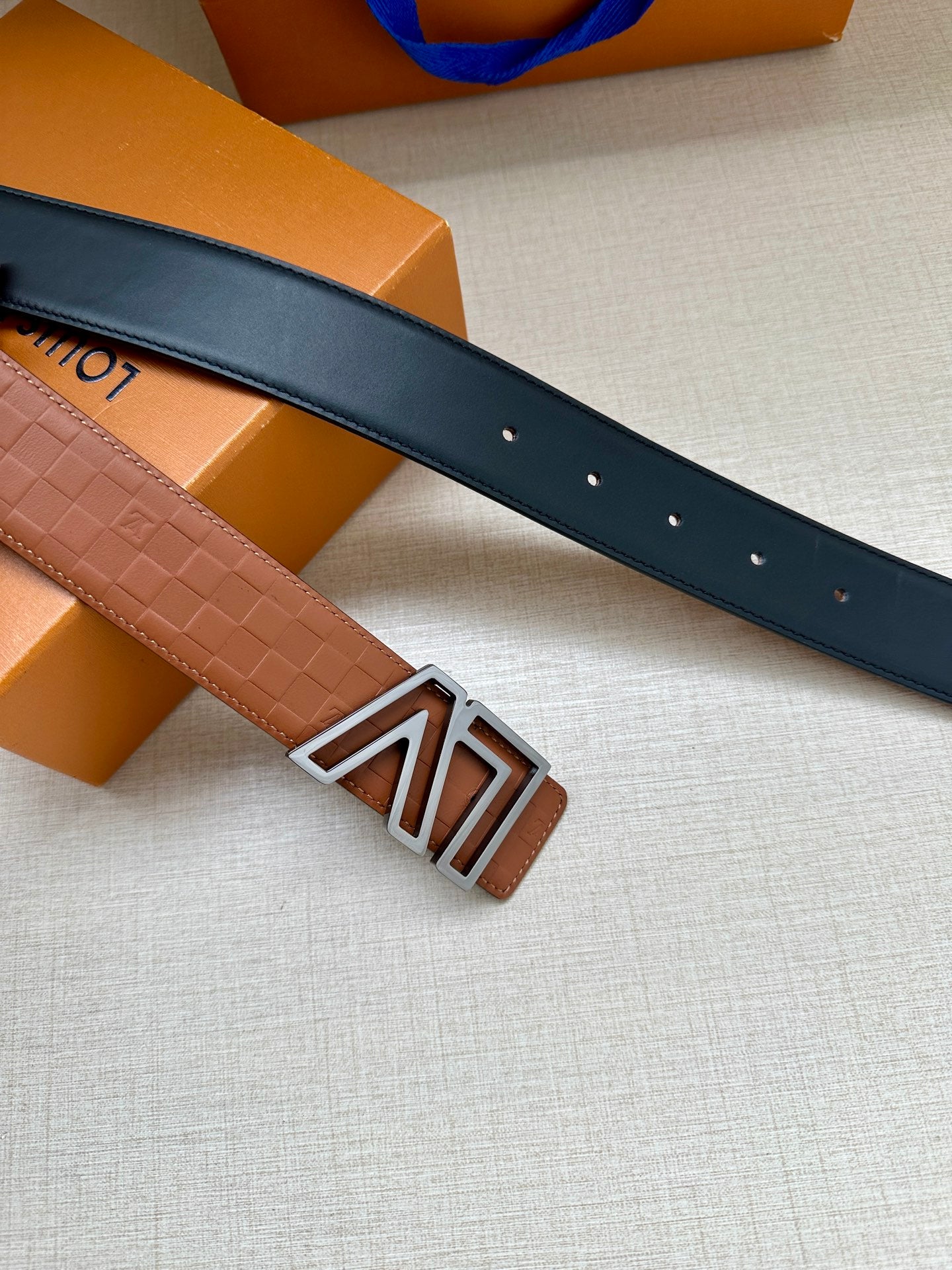 Dark leather belt with prong holes and silver-tone LV buckle, angled view