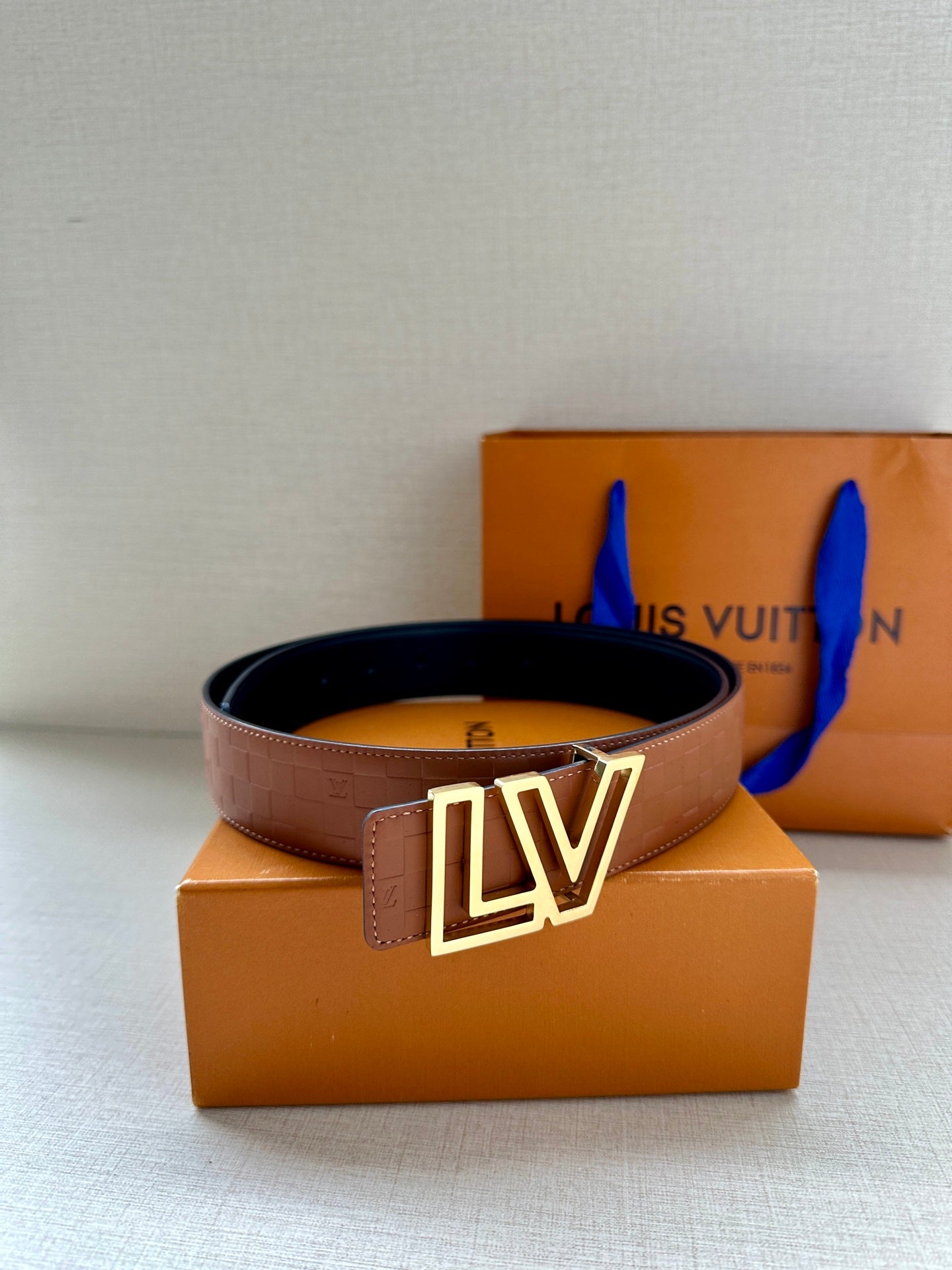 Brown leather belt with gold-tone LV buckle and coiled profile