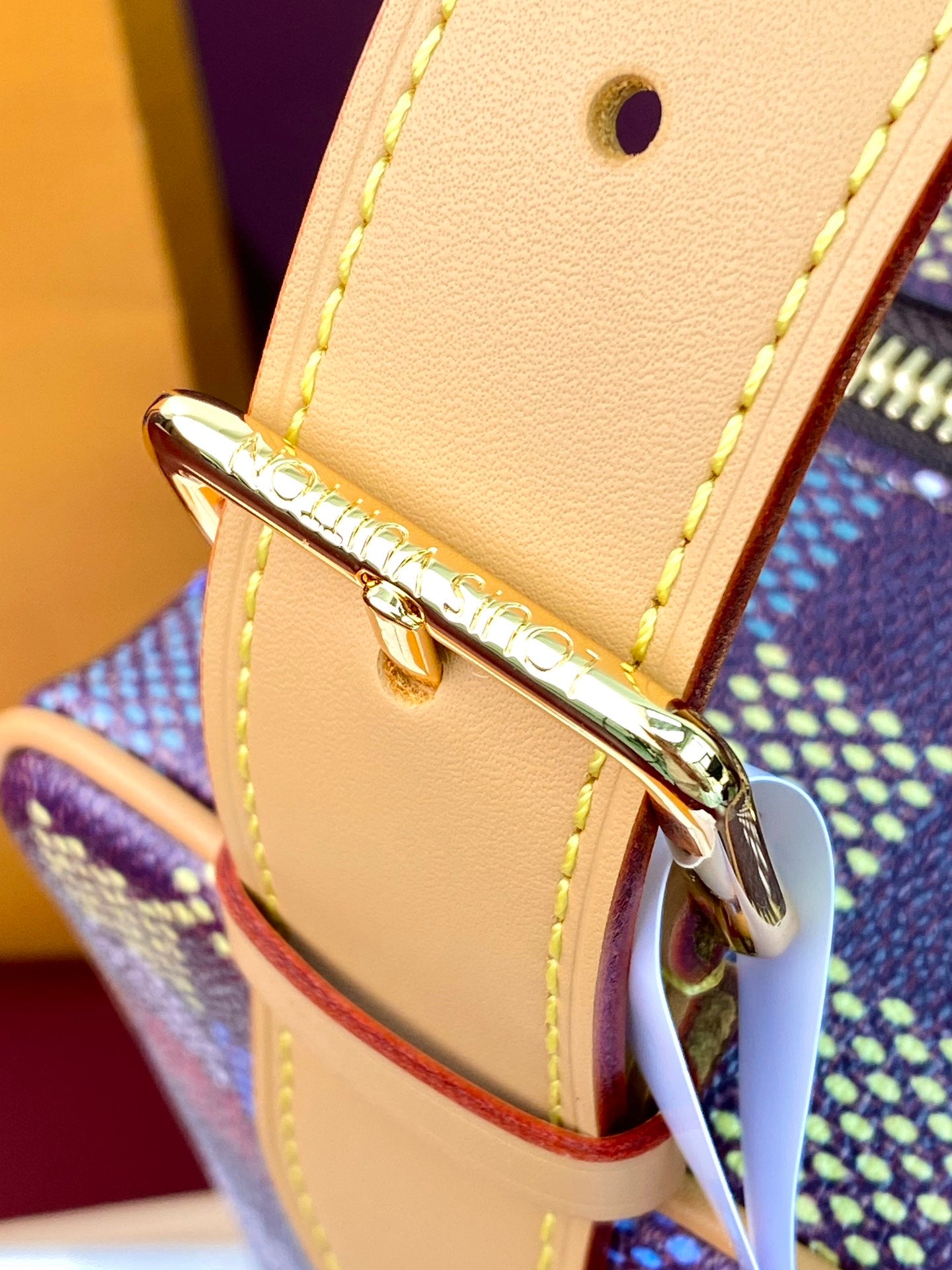Tan leather strap loop with gold buckle hardware on check-pattern bag