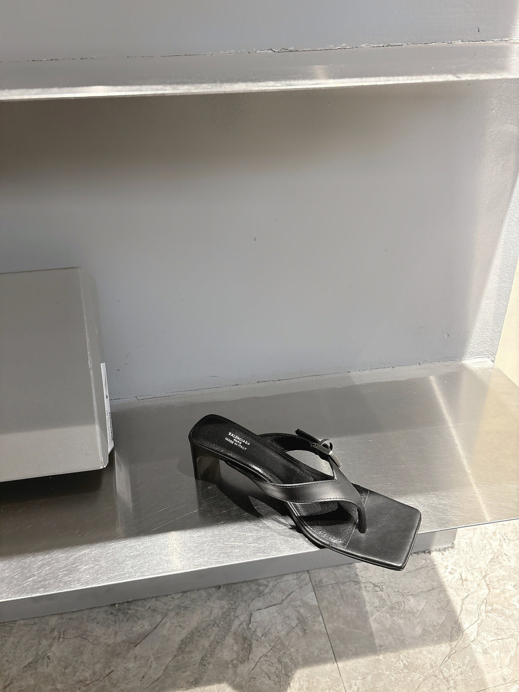 Balenciaga black leather sandals with buckle strap, angled side view on display shelf