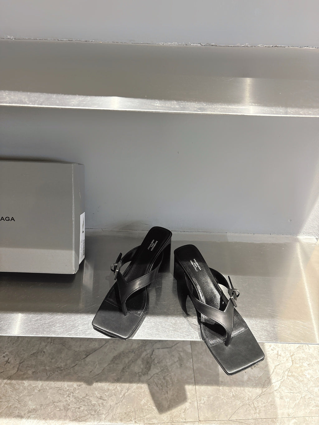 Balenciaga black leather sandals with square toe and buckle strap detail, angled on shelf
