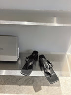 Balenciaga black leather sandals with square toe and buckle strap detail, angled on shelf