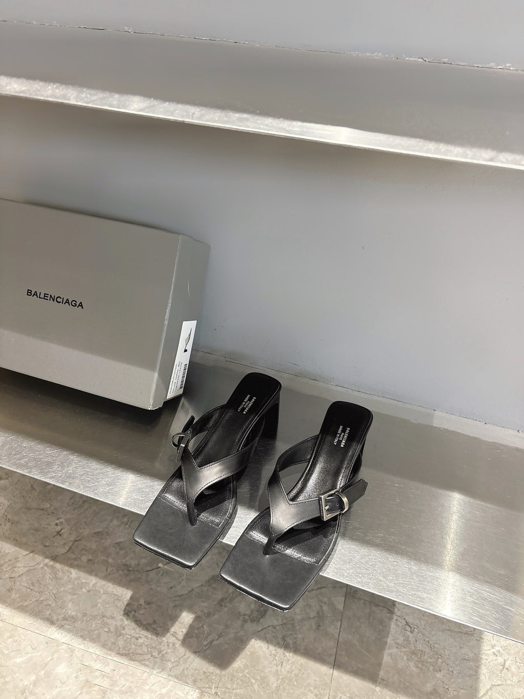 Balenciaga black leather sandals with square toe and silver buckle, front view on shelf