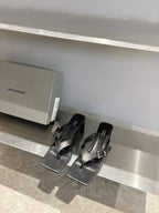 Balenciaga black leather sandals with square toe and silver buckle, front view on shelf
