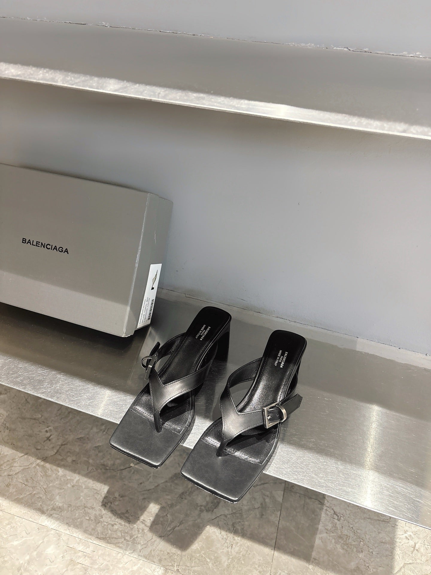 Balenciaga black leather sandals with square toe and silver buckle, front view on shelf