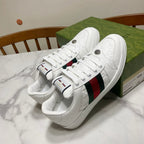 White Gucci lace-up sneakers with green-red web stripe and metal logo buttons on side.