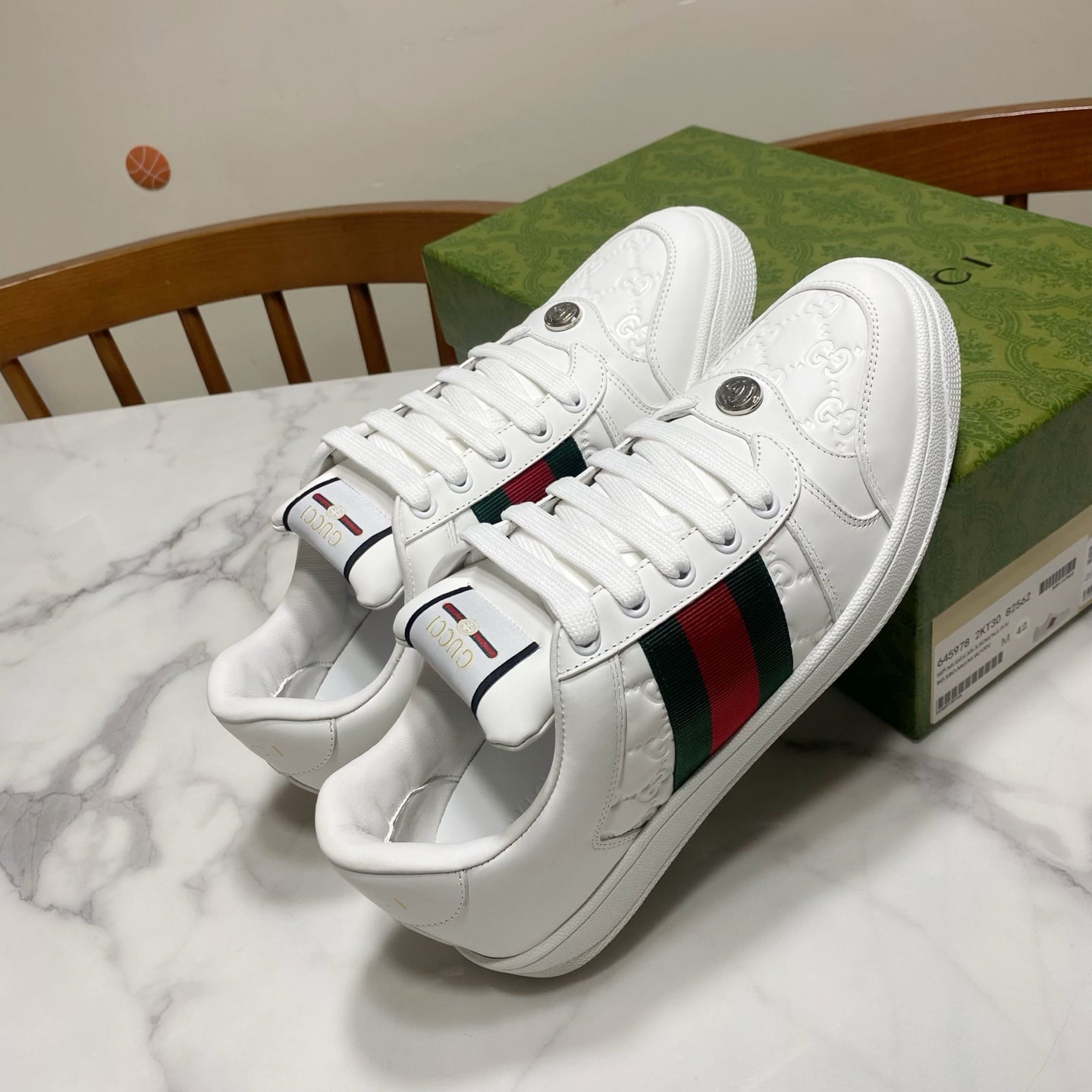 White Gucci lace-up sneakers with green-red web stripe and metal logo buttons on side.