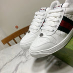 White Gucci lace-up sneakers with green-red web stripe, stitched panels, and rubber sole.