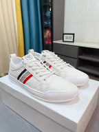 White luxury sneakers on display, lace-up with Greek key side stripe and red accent.