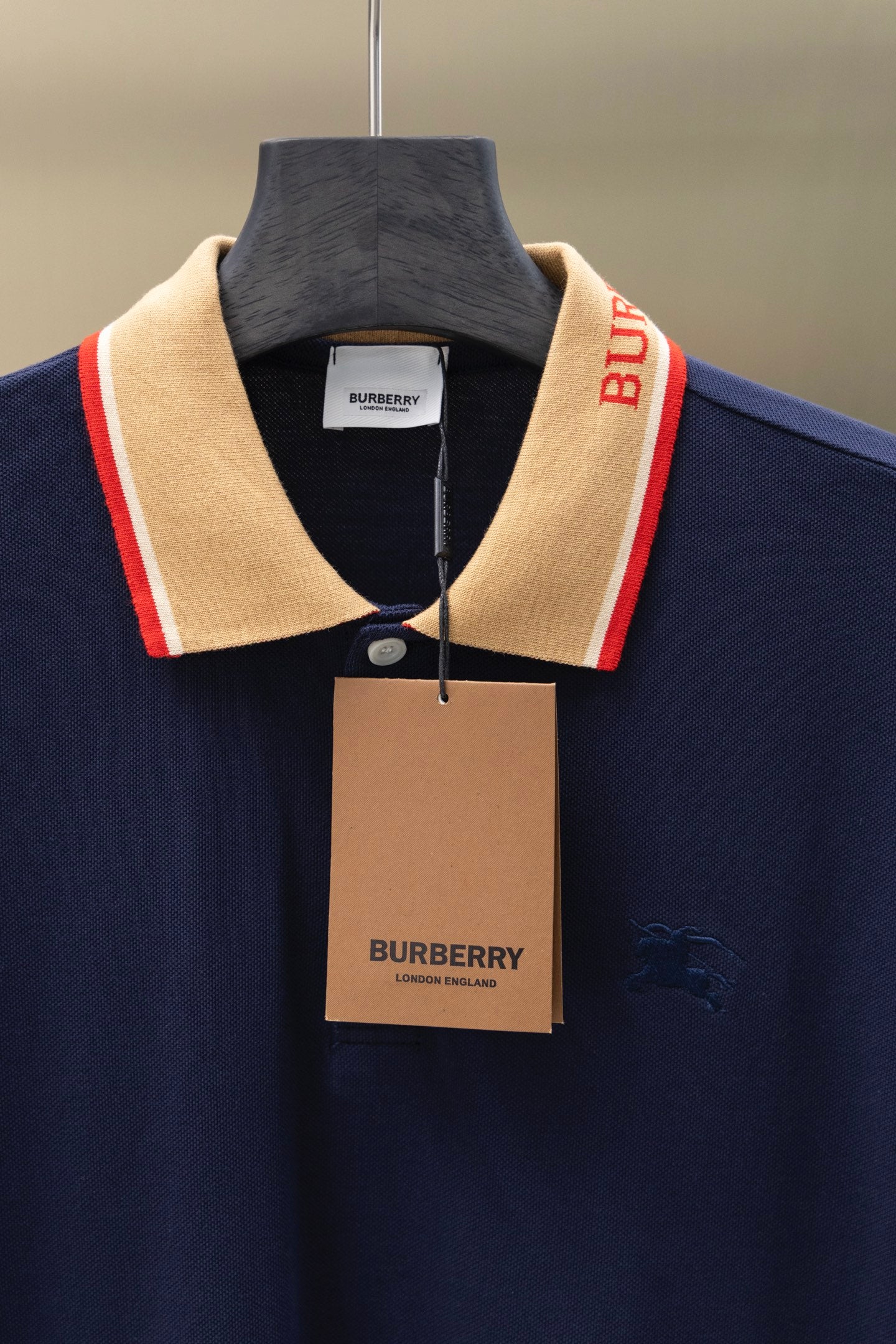 Navy polo shirt with beige collar trim, button placket, hanging brand tag