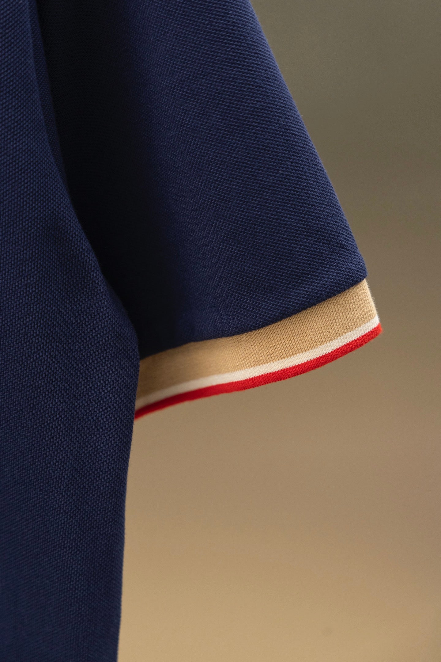Navy polo shirt sleeve hem with beige band and red stripe